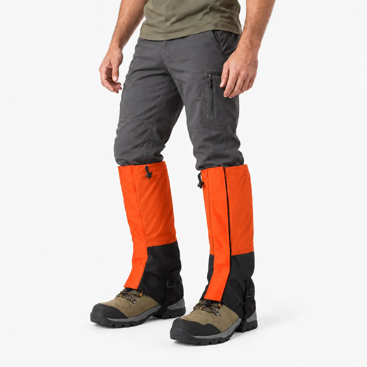 Oranje gamaschen met zwart onderstuk, schuin van opzij gedragen over wandelschoenen en een grijze broek, tegen een witte achtergrond. 4
