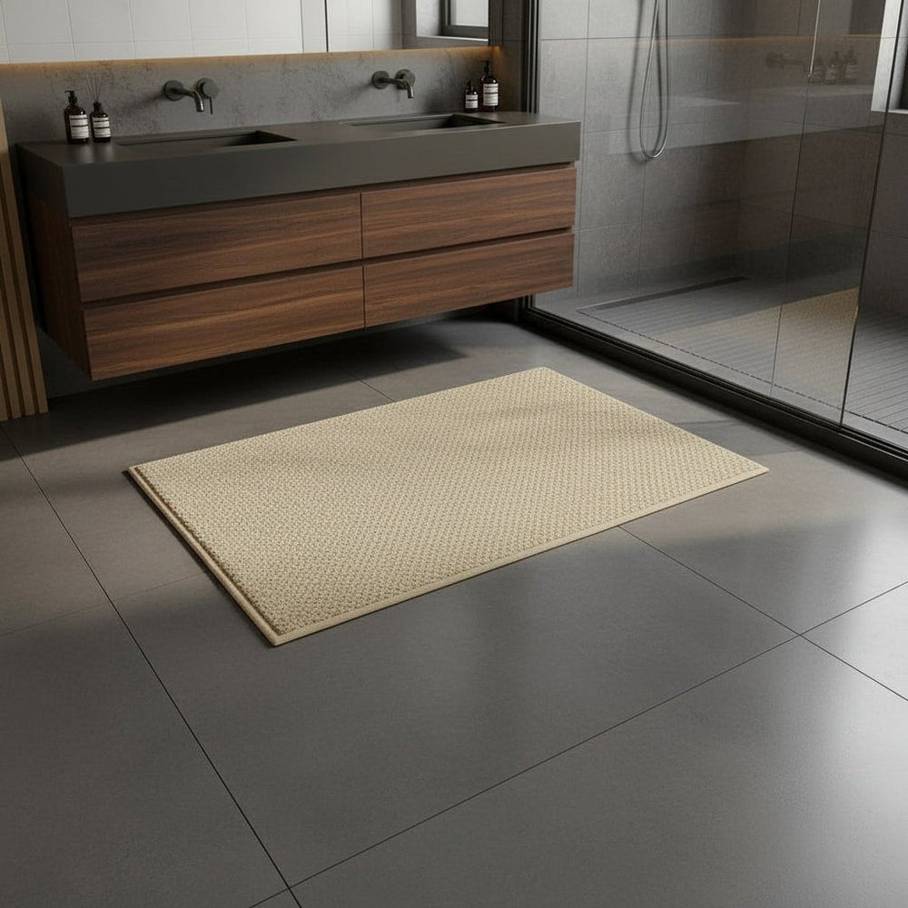 Beige badmat voor een zwevend houten wastafelmeubel en glazen douchewand op grijze tegels 2