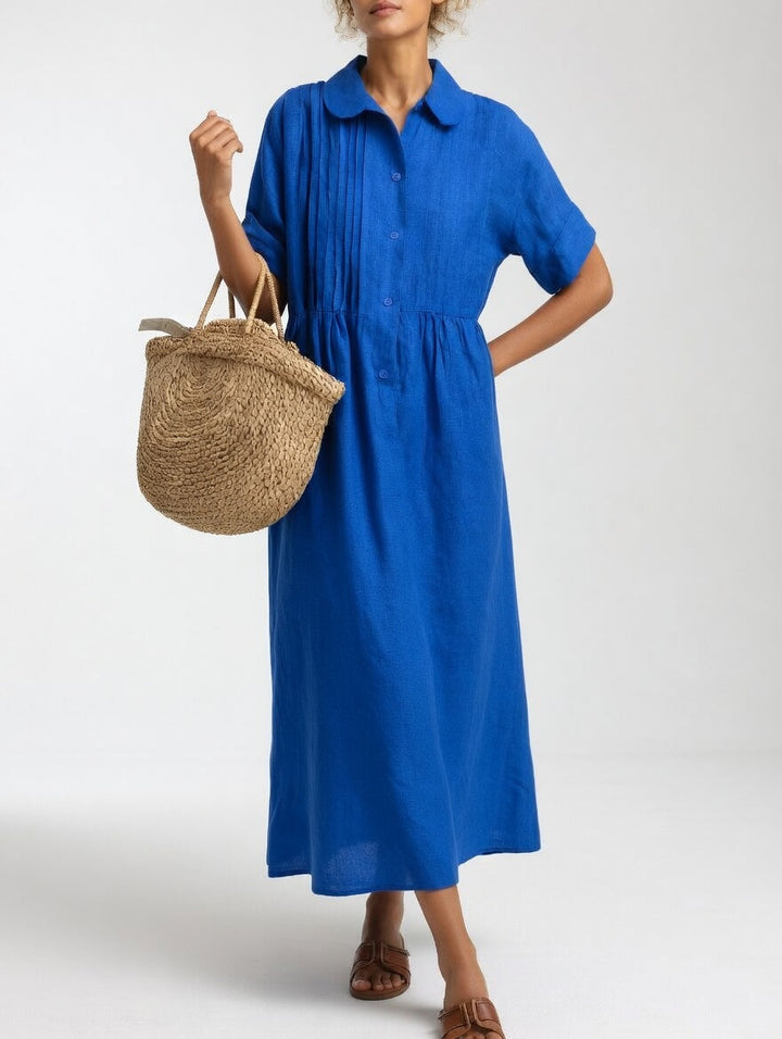 Model draagt de felblauwe uitvoering van voren, met een hand in de zij en een rieten tas aan de arm. 3