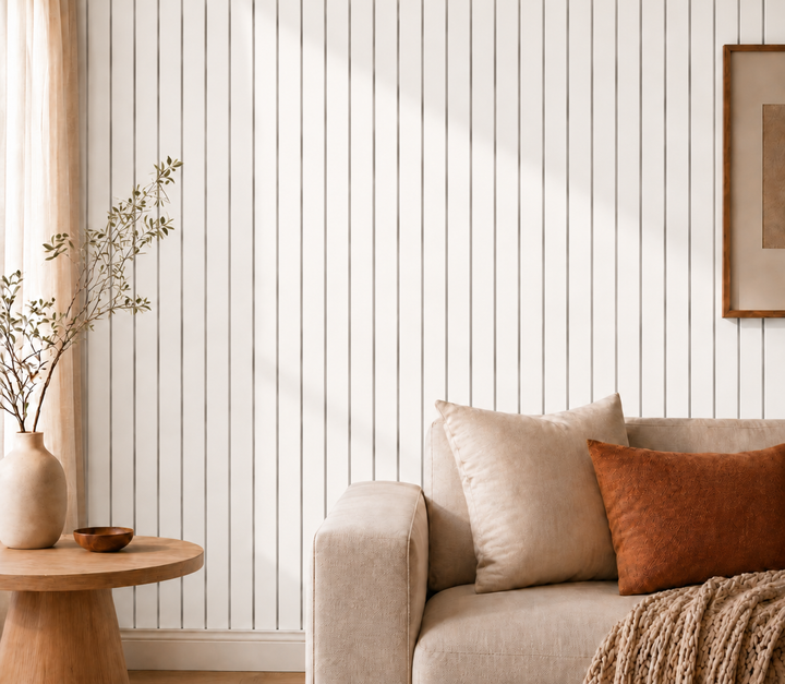 Wit lattenpaneel als accentwand achter een beige bank met kussens, ronde bijzettafel en vaas 21