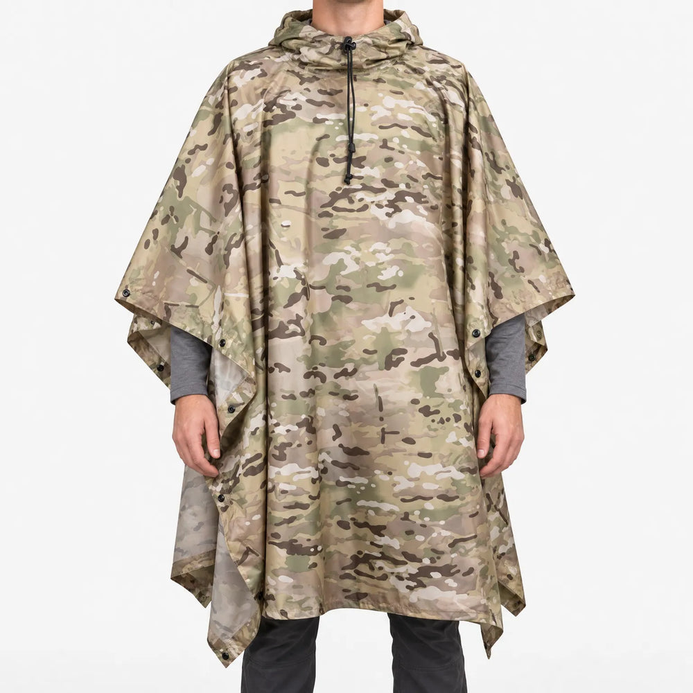 Voorkant van de poncho in beige, groen en bruin camouflageprint op een witte achtergrond, gedragen door een model met capuchon en drukknopen. 2