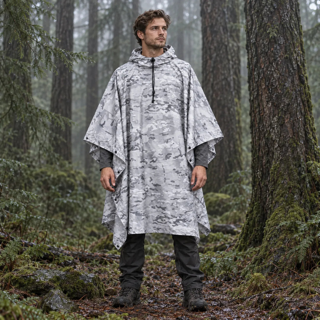 Model staat in een mistig naaldbos in de poncho met grijs-witte camouflageprint, capuchon op en zijkanten dichtgeknoopt. 3
