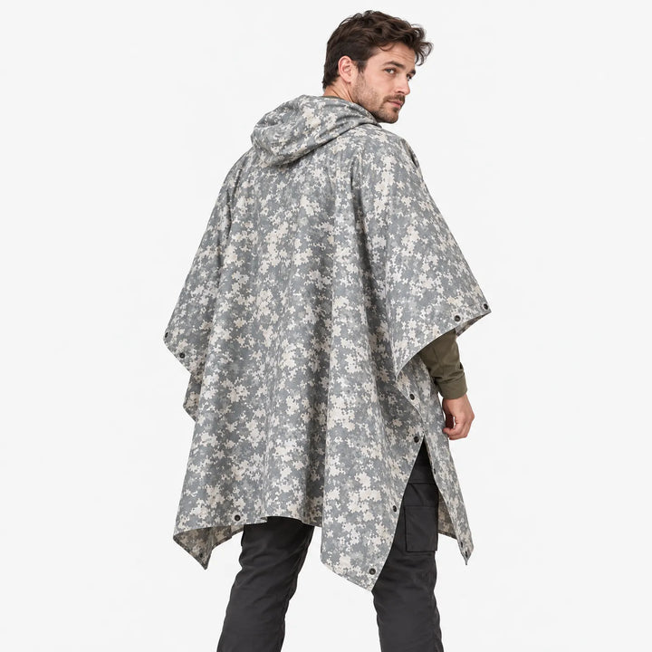Achterkant van de poncho in grijs-beige pixelcamouflage, gedragen door een model dat over zijn schouder kijkt, met capuchon en drukknopen. 4