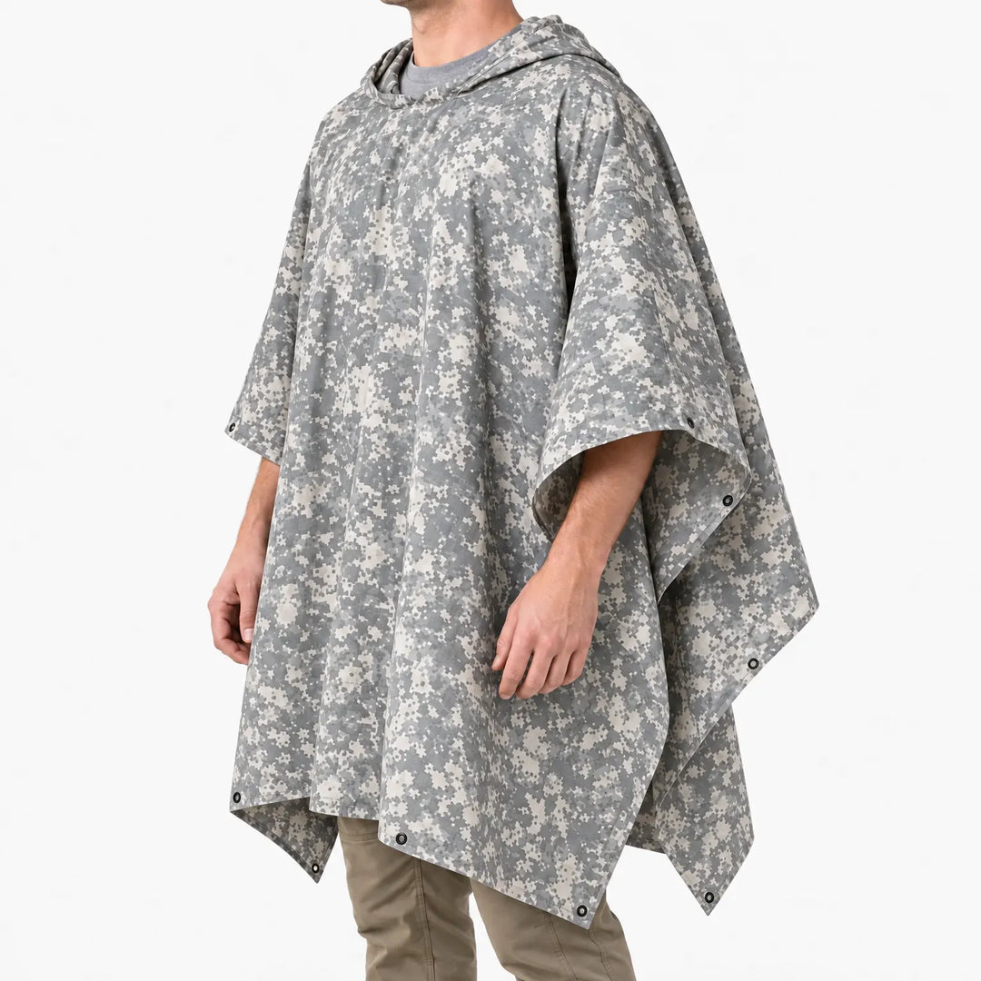 Schuin zijaanzicht van de poncho in grijs-beige pixelcamouflage met capuchon en metalen oogjes langs de randen, gedragen door een model. 5