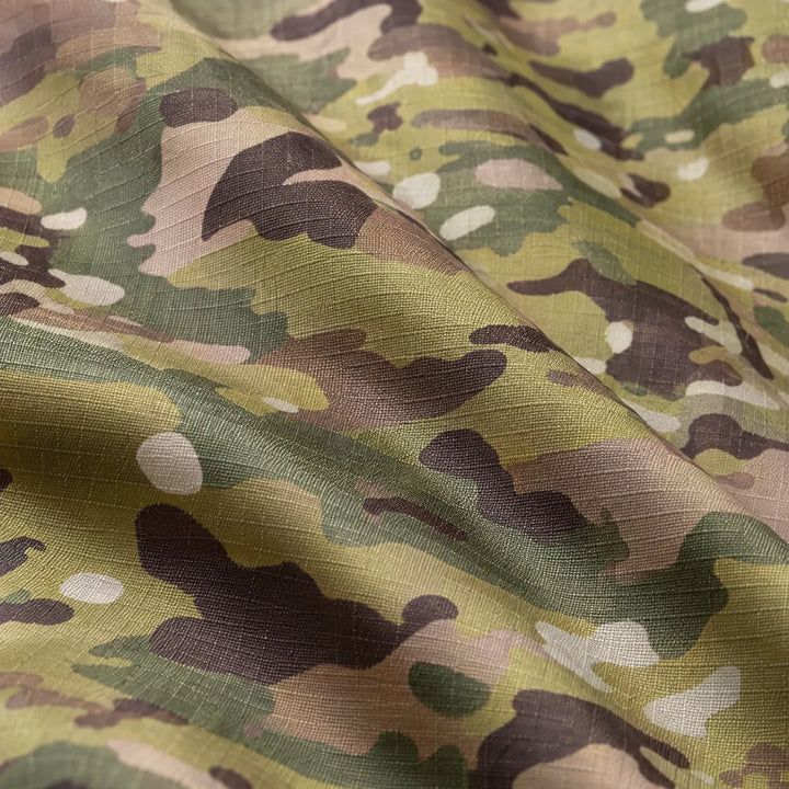 Close-up van de stof met groen-bruine camouflageprint, waarop de geweven ripstop-structuur en de plooien van het materiaal goed te zien zijn. 6