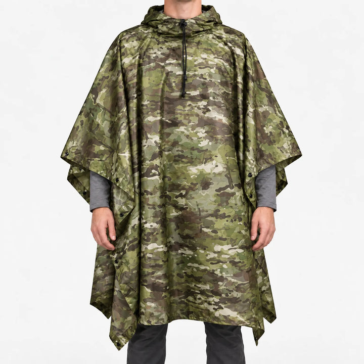 Voorkant van de poncho in groene camouflageprint met bruine en beige vlekken, gedragen door een model op een witte achtergrond. 7