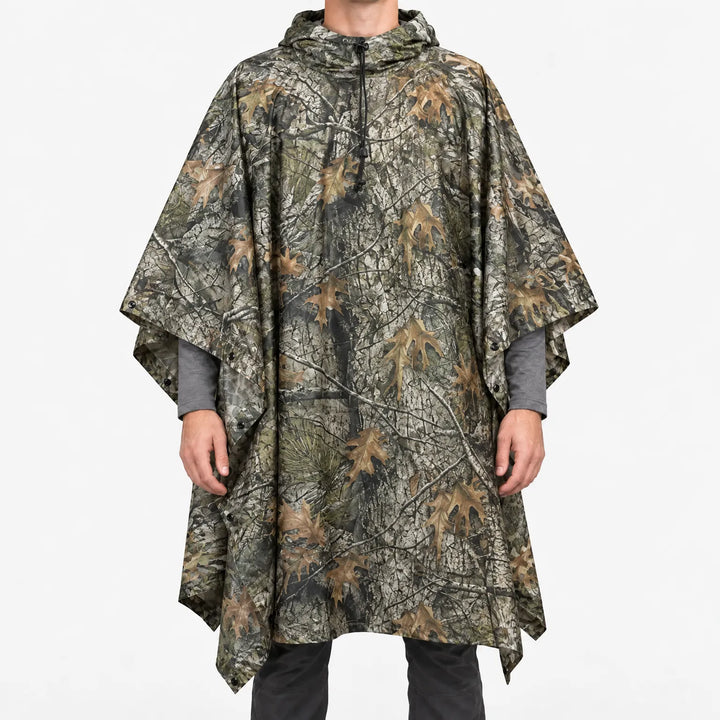 Voorkant van de poncho met boomschors- en eikenbladeren-camouflageprint in grijs, bruin en groen, gedragen door een model. 9