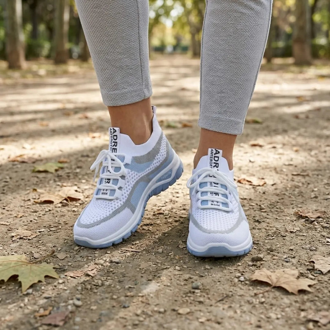 Witte sneakers met blauwe zool, gedragen op een bospad met herfstbladeren, gecombineerd met een grijze legging. 2