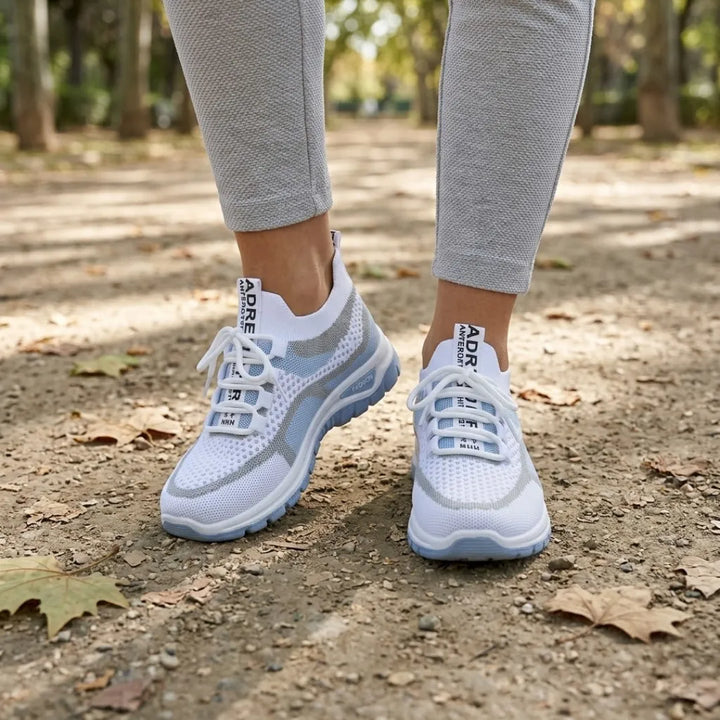 Witte sneakers met blauwe zool, gedragen op een bospad met herfstbladeren, gecombineerd met een grijze legging. 2