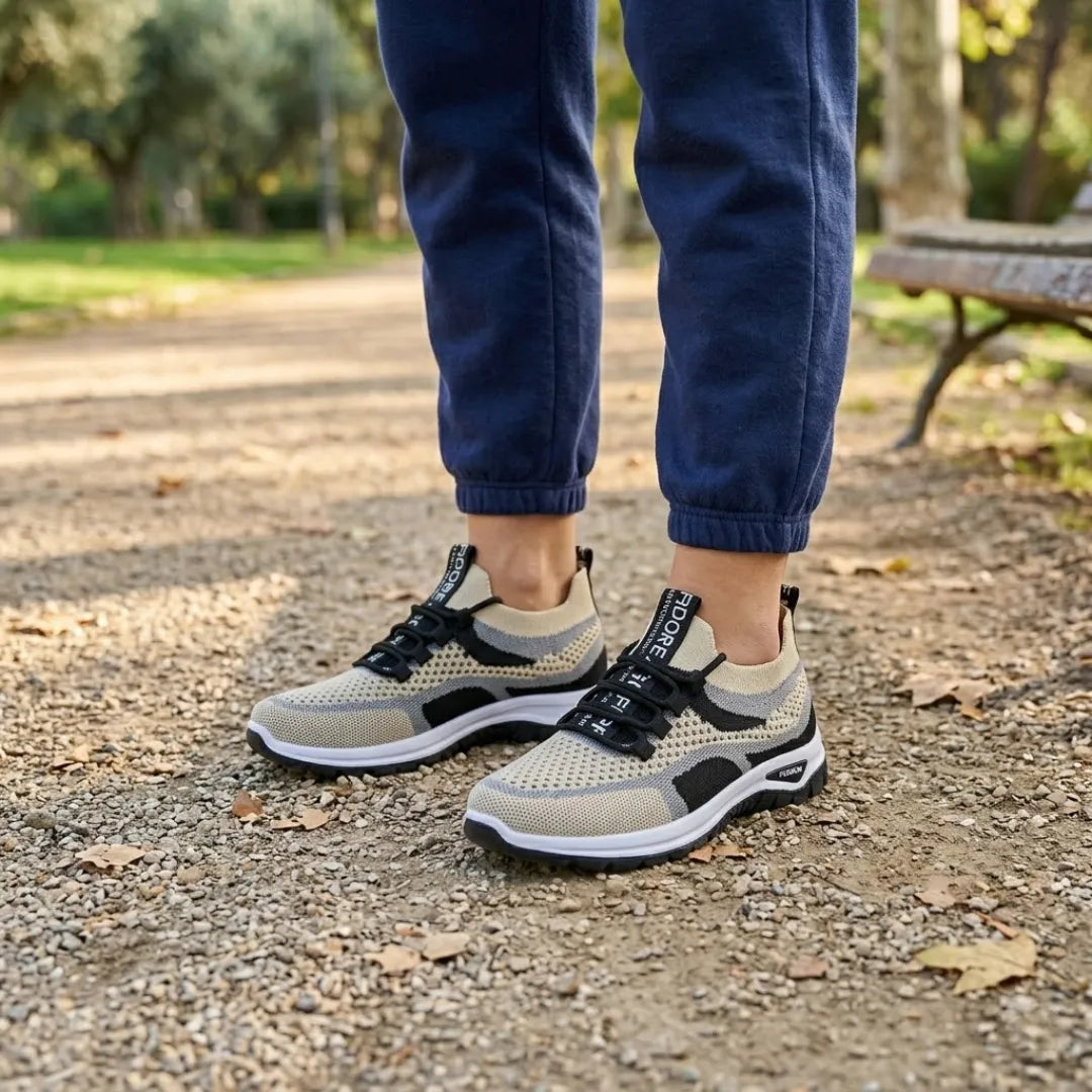 Model draagt de beige sneakers met zwarte en grijze accenten en zwarte veters op een grindpad in een park. 38