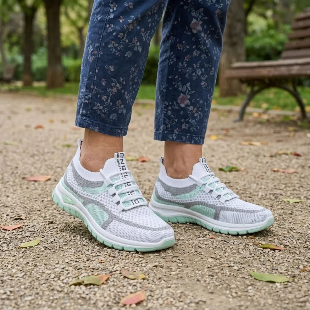 Witte sneakers met mintgroene zool, gedragen in een park met een gebloemde blauwe broek, een bankje en herfstbladeren. 11