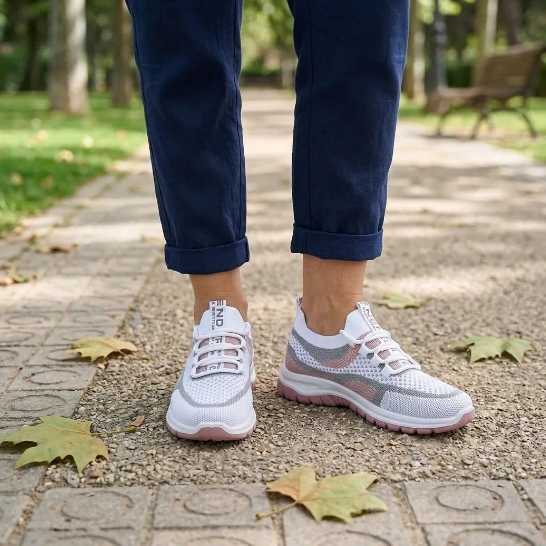 Witte sneakers met roze zool, gedragen op een parkpad met een donkerblauwe broek en herfstbladeren. 20