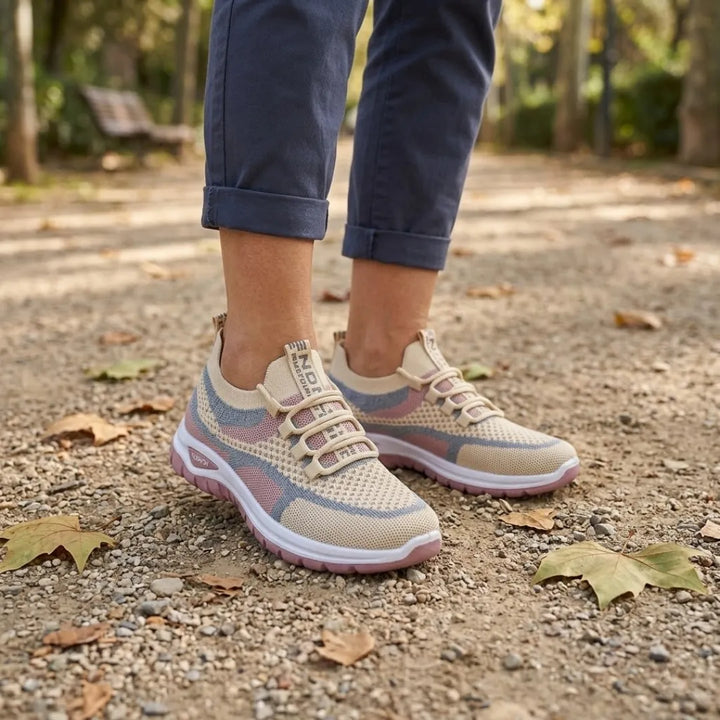 Model draagt de beige sneakers met roze en blauwgrijze accenten tijdens een wandeling over een grindpad met herfstbladeren. 29
