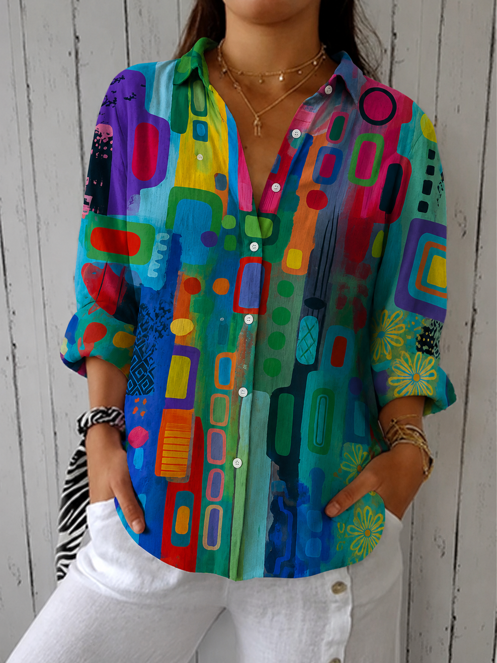 Vooraanzicht van de blouse in een regenboog van fel groen, blauw, rood en paars, met knoopsluiting en kraag, gedragen met witte broek. 2