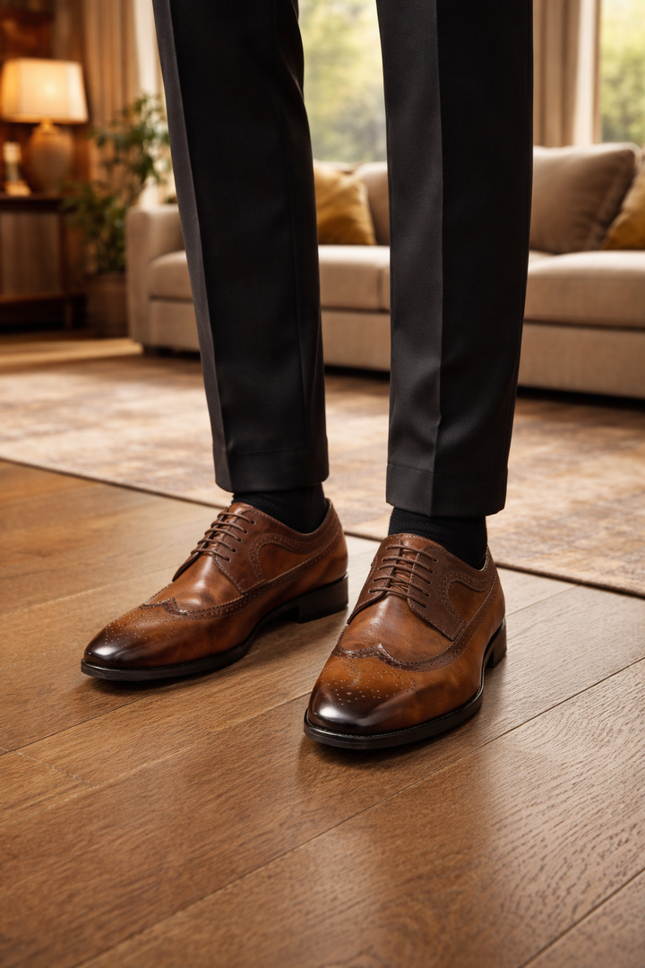Bruine brogues gedragen met zwarte pantalon en zwarte sokken, staand op een houten vloer in een warme woonkamer. 1