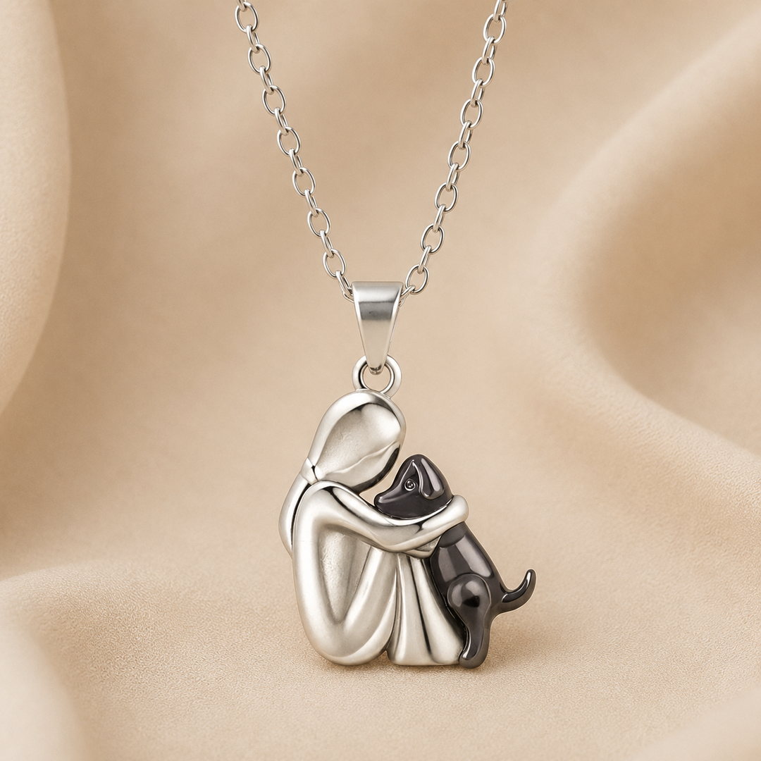 Zilverkleurige hanger van een figuur die een zwarte hond omarmt, aan een fijne schakelketting op beige satijn. 3