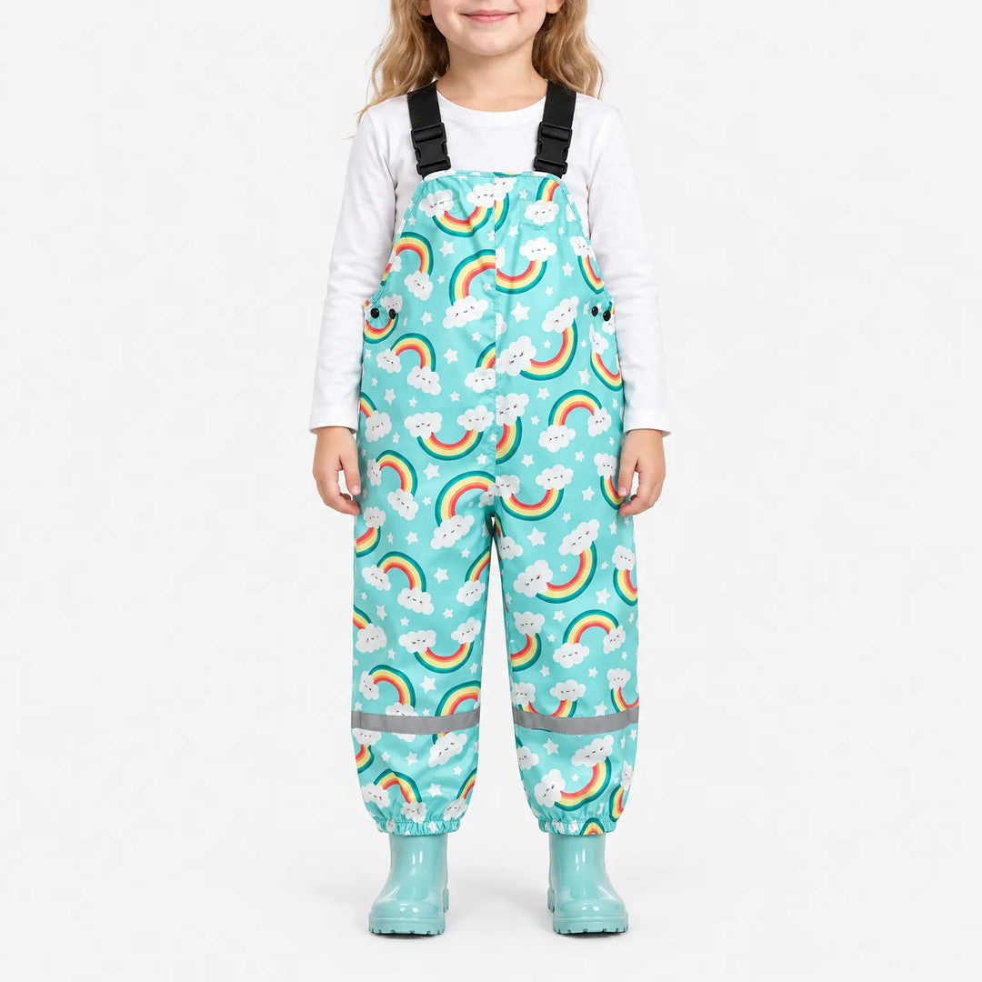 Meisje draagt turquoise tuinbroek met regenbogen en lachende wolkjes, reflecterende strepen onderaan en turquoise laarzen, op witte achtergrond. 2