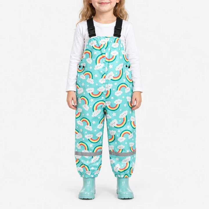 Meisje draagt turquoise tuinbroek met regenbogen en lachende wolkjes, reflecterende strepen onderaan en turquoise laarzen, op witte achtergrond. 2