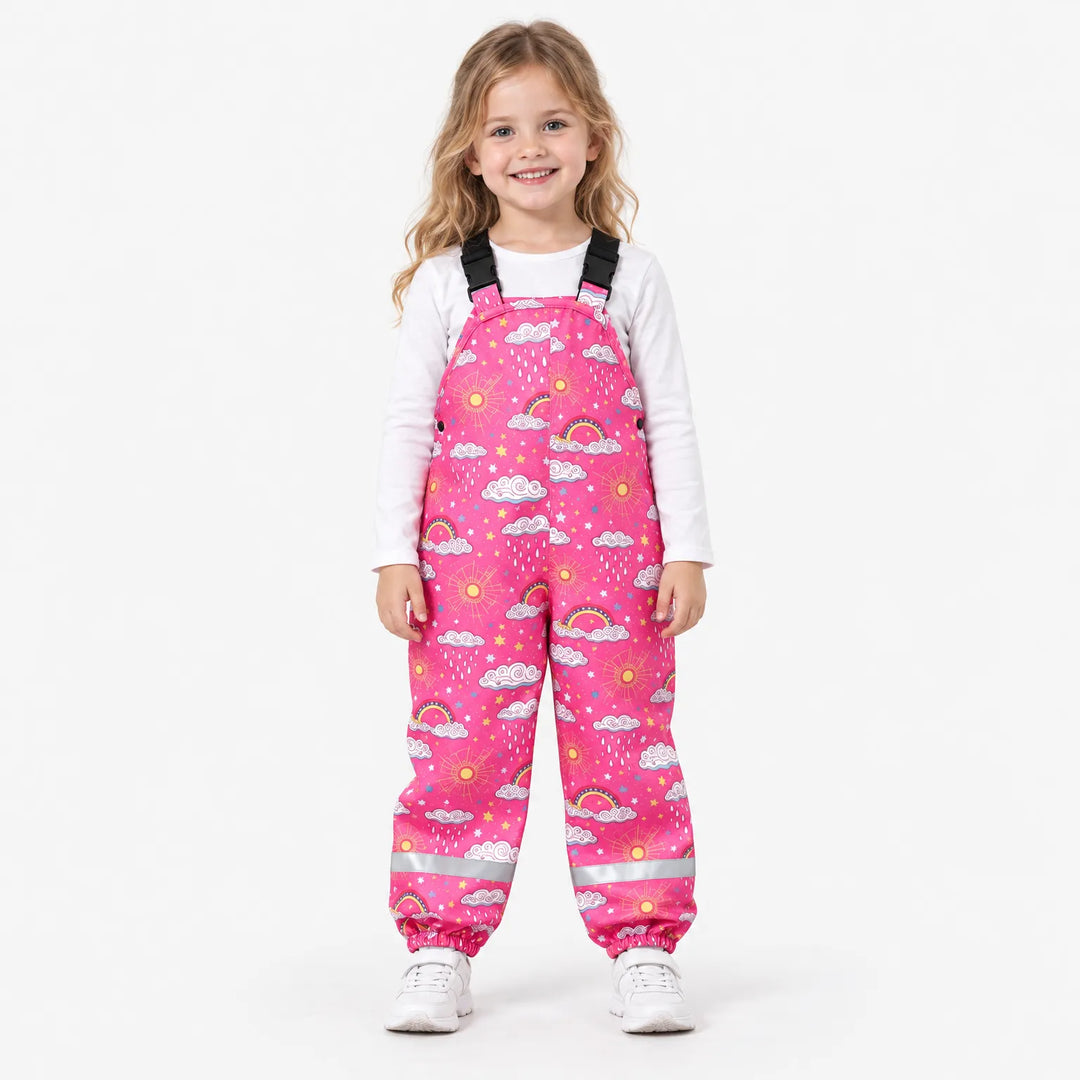 Lachend meisje in roze tuinbroek met wolken, zonnetjes en regenboogjes, met witte sneakers en reflecterende strepen. 4