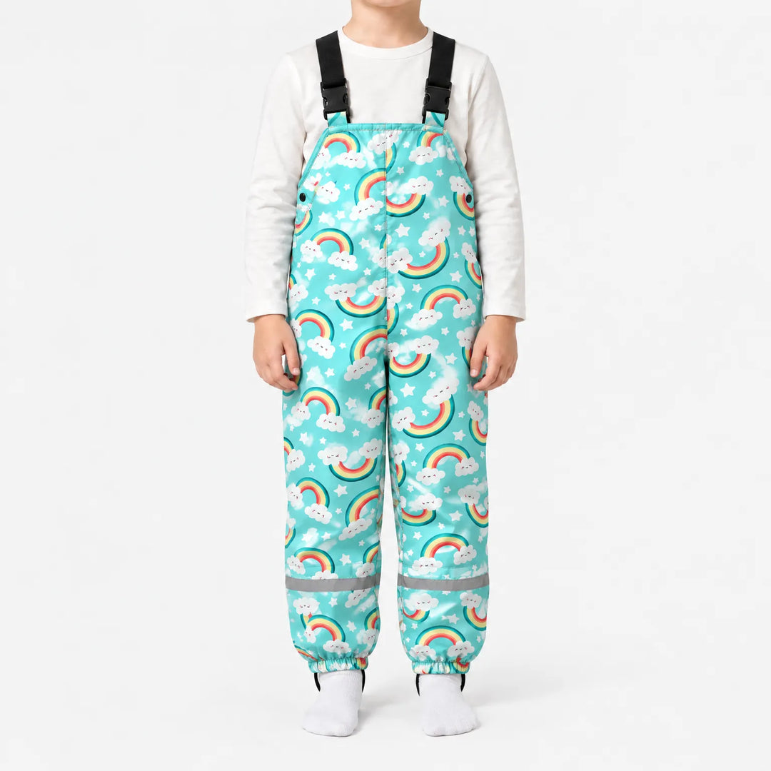 Kind draagt turquoise tuinbroek met regenbogen, wolkjes en sterren, met zwarte bretels en reflecterende strepen. 8