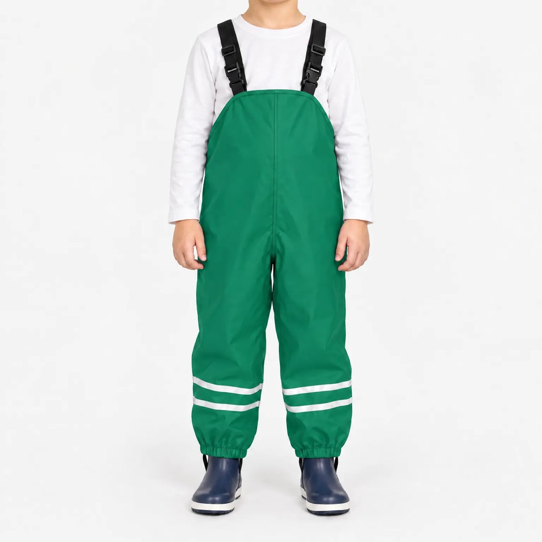 Kind draagt groene tuinbroek met reflecterende banden en elastische enkelbanden, met wit shirt en donkerblauwe laarsjes. 10