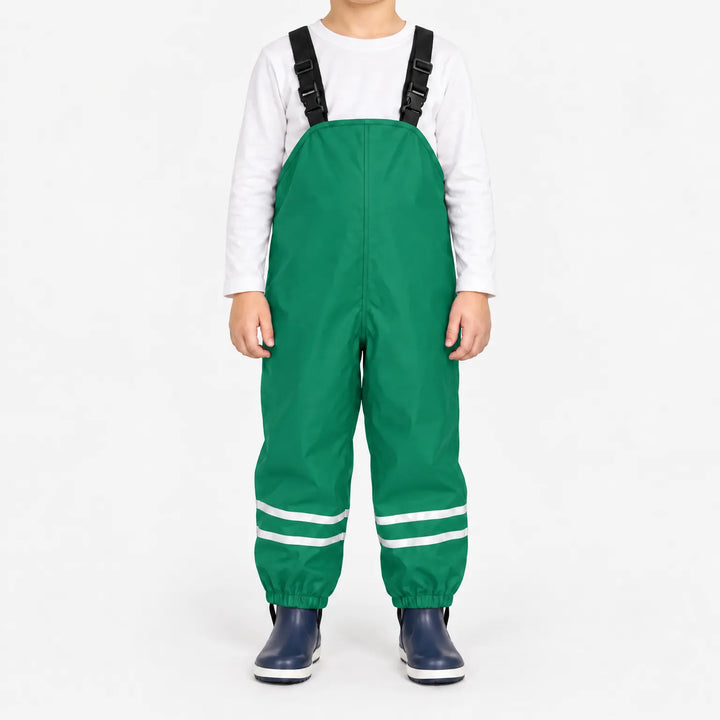 Kind draagt groene tuinbroek met reflecterende banden en elastische enkelbanden, met wit shirt en donkerblauwe laarsjes. 10