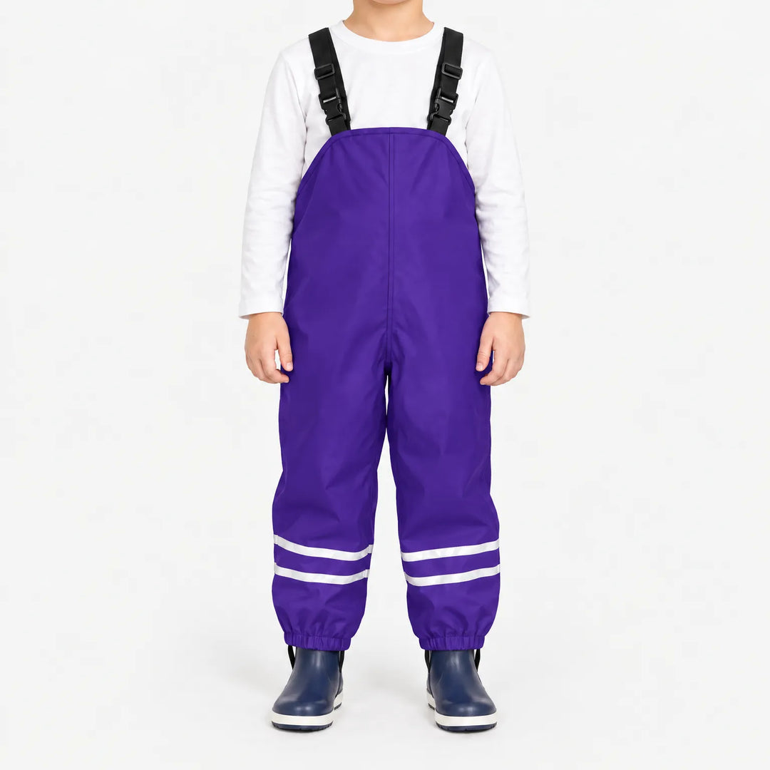 Kind draagt paarse tuinbroek met reflecterende banden en zwarte bretels, met wit shirt en donkerblauwe rubberlaarsjes. 12