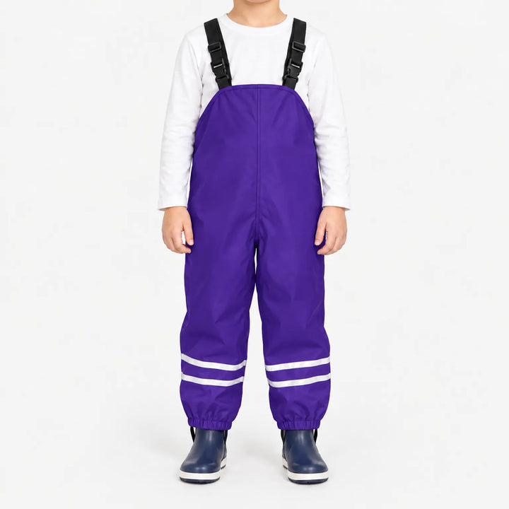 Kind draagt paarse tuinbroek met reflecterende banden en zwarte bretels, met wit shirt en donkerblauwe rubberlaarsjes. 12