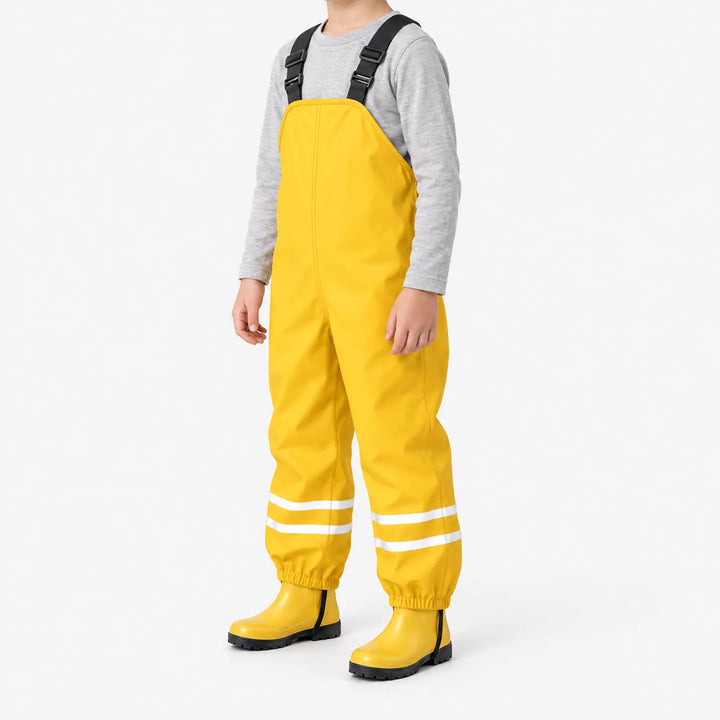 Kind draagt gele tuinbroek met reflecterende banden in driekwartaanzicht, met grijs shirt en gele rubberlaarsjes. 5