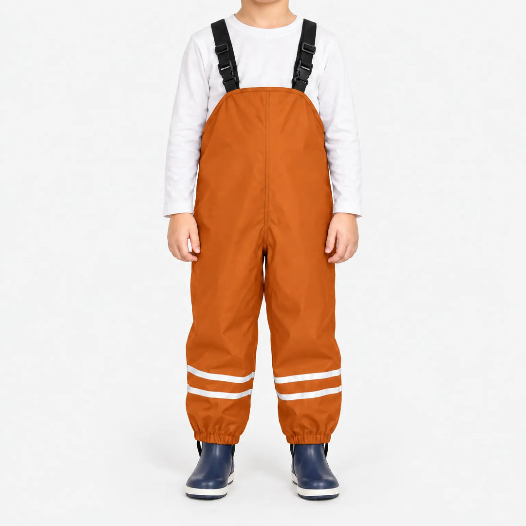 Kind draagt oranje tuinbroek met reflecterende banden, wit shirt en donkerblauwe rubberlaarsjes, vooraanzicht op witte achtergrond. 8