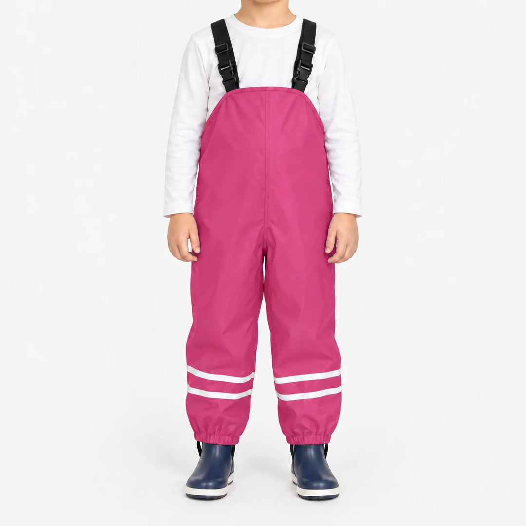 Kind draagt roze tuinbroek met reflecterende banden en zwarte bretels, met wit shirt en donkerblauwe laarsjes. 9