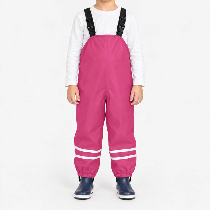 Kind draagt roze tuinbroek met reflecterende banden en zwarte bretels, met wit shirt en donkerblauwe laarsjes. 9