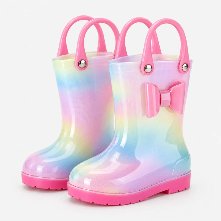 Paar regenlaarzen met pastelregenboogprint, roze strik en twee roze handvatten per laars, schuin van voren op witte achtergrond. 2