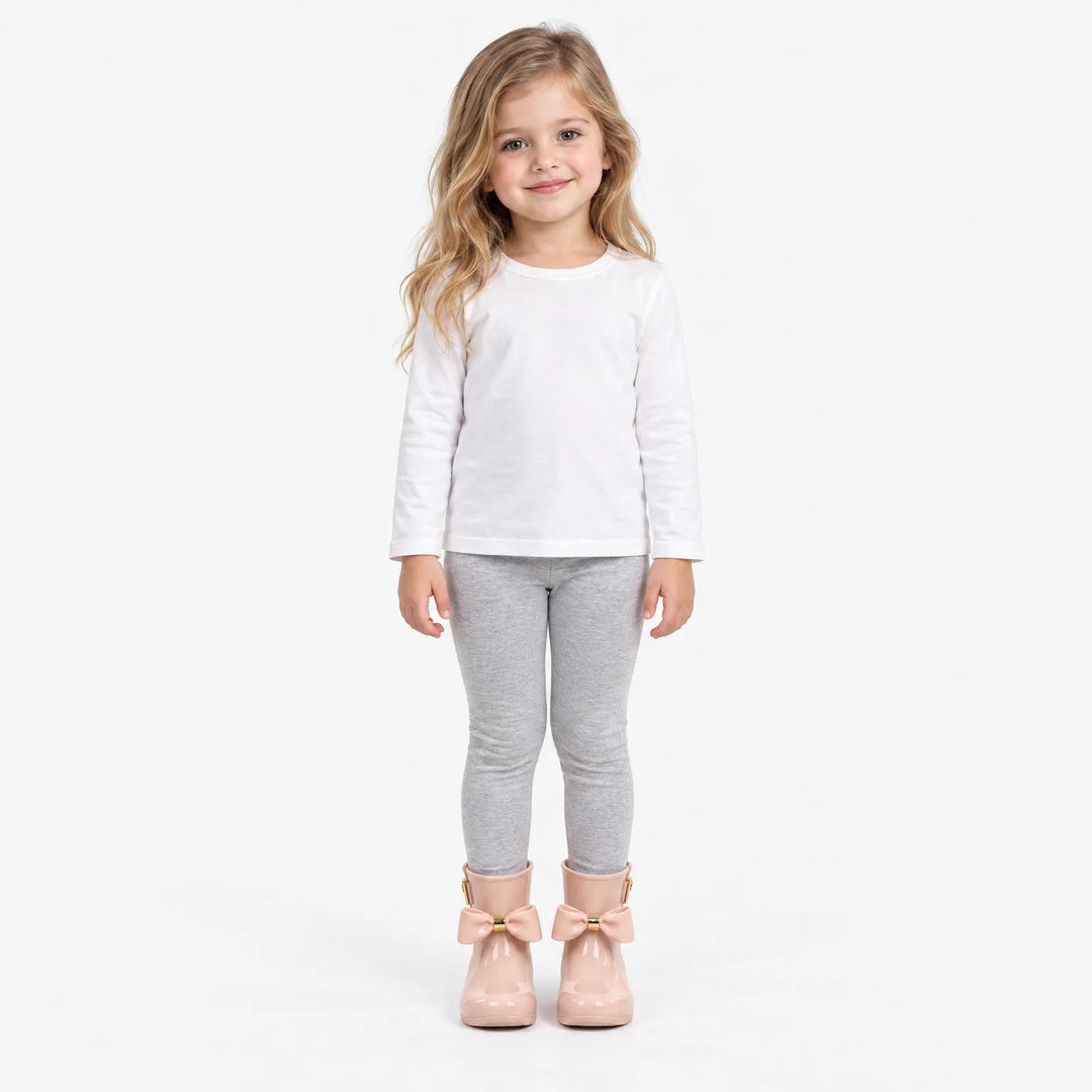Glimlachend meisje in wit shirt en grijze legging draagt roze laarsjes met strik, volledig staand op een witte achtergrond. 4