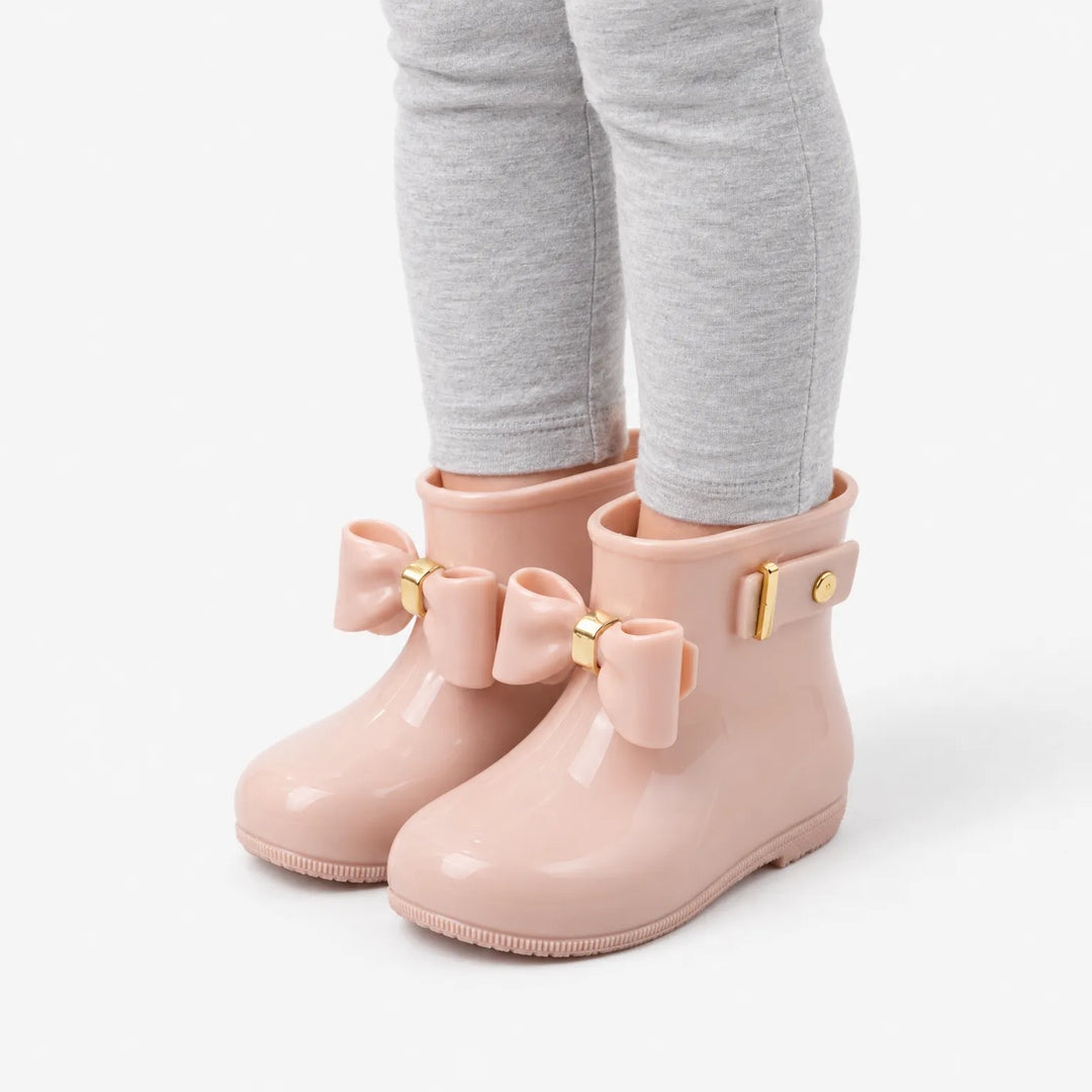 Schuin zijaanzicht van roze glanzende laarsjes met strik en gouden gesp, gedragen onder een grijze legging. 5