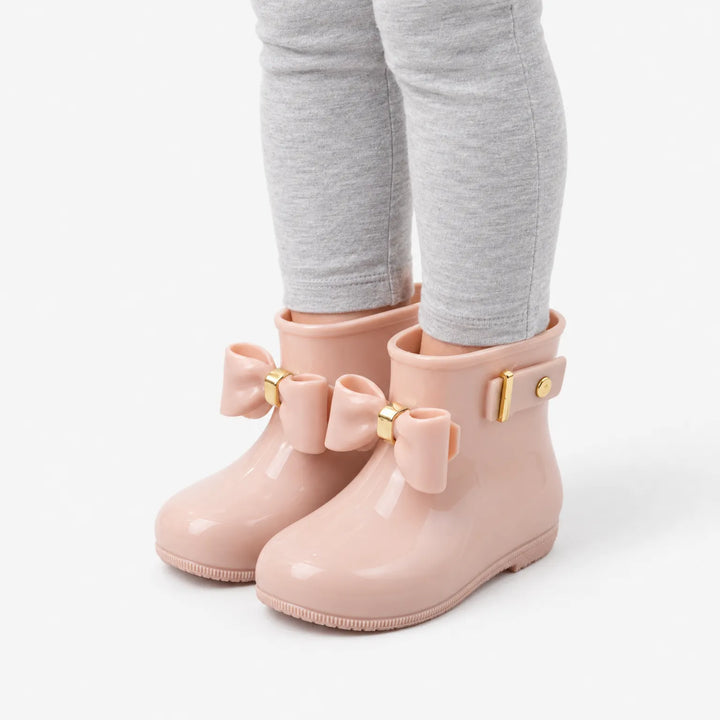 Schuin zijaanzicht van roze glanzende laarsjes met strik en gouden gesp, gedragen onder een grijze legging. 5