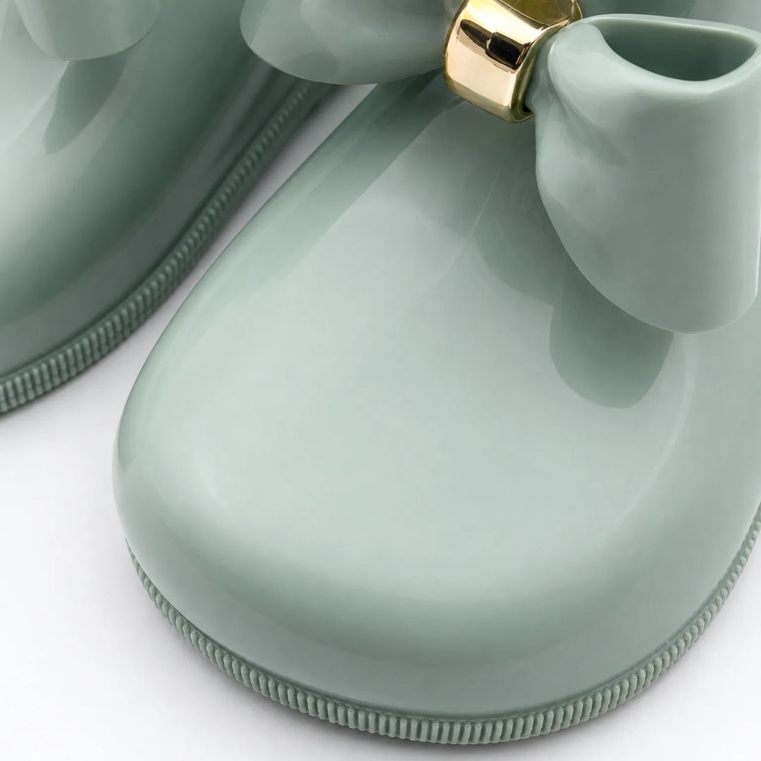 Close-up van de ronde neus en geribbelde zool van een mintgroene glanzende laars met strik en gouden ring. 6
