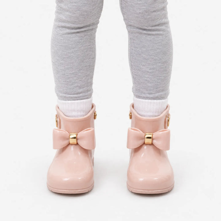 Voorkant van roze laarsjes met gouden strikdetail, gedragen met witte sokken en een grijze legging. 7