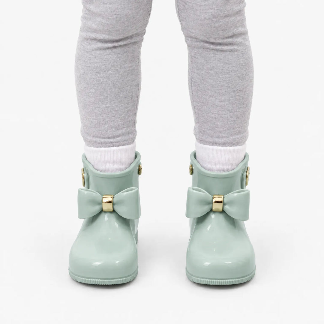 Voorkant van mintgroene glanzende laarsjes met strik en gouden detail, gedragen met witte sokken en grijze legging. 8