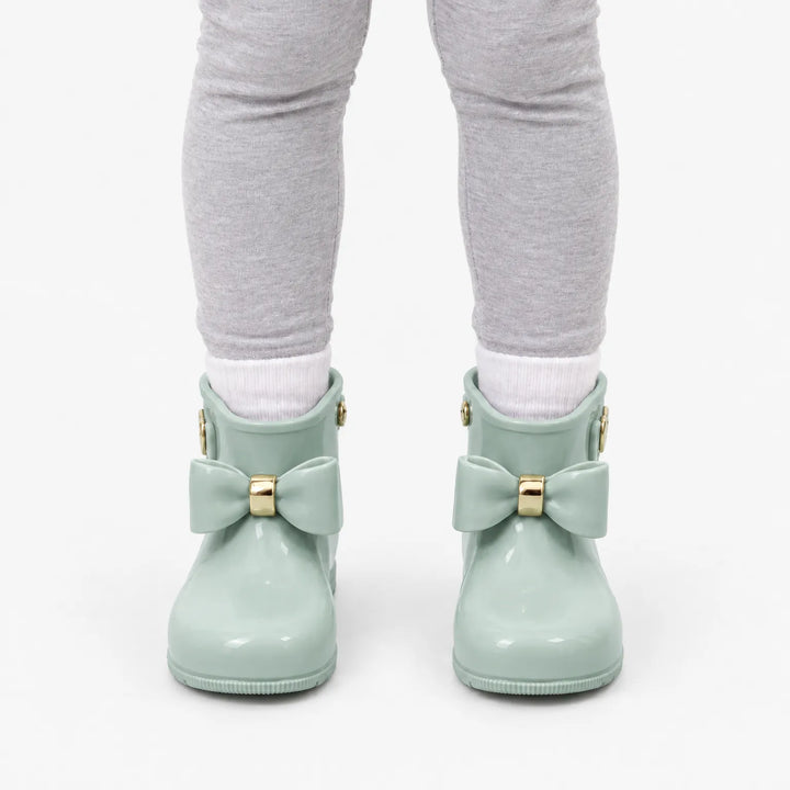 Voorkant van mintgroene glanzende laarsjes met strik en gouden detail, gedragen met witte sokken en grijze legging. 8
