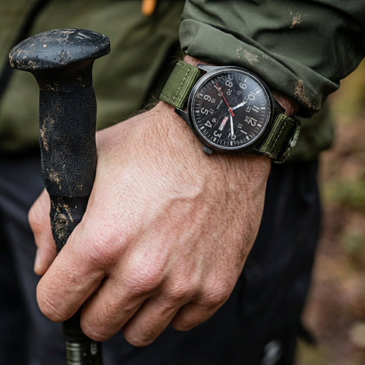 Horloge met groene stoffen band om de pols van een wandelaar die een modderige wandelstok vasthoudt, in het bos. 2