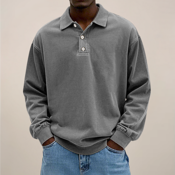 Model draagt het poloshirt in grijs, voorkant met knoopsluiting, boordjes aan de mouwen en een spijkerbroek. 7