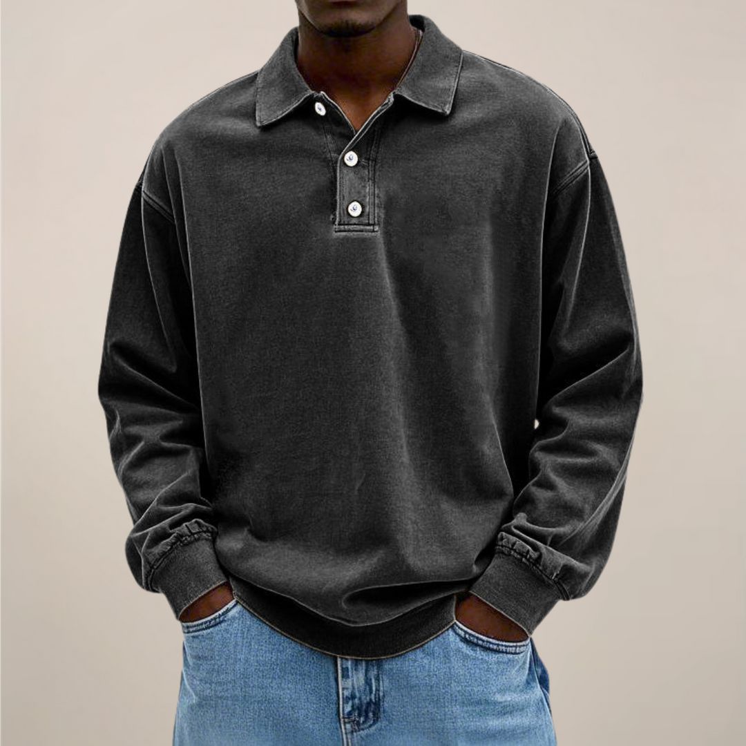 Model draagt het poloshirt in zwart, voorkant met kraag en drie knopen, handen in de zakken van een spijkerbroek. 8