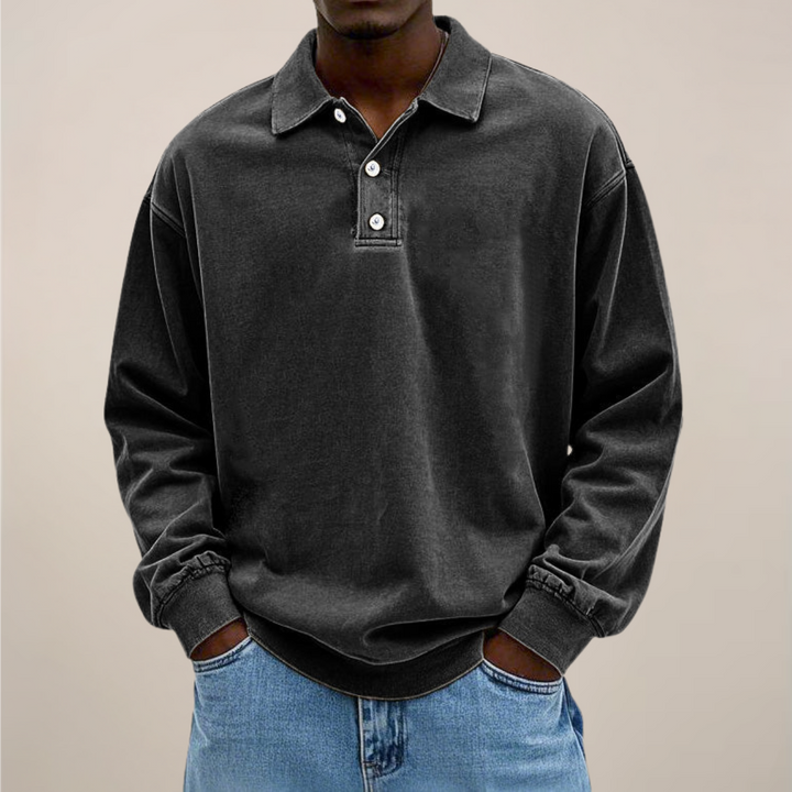 Model draagt het poloshirt in zwart, voorkant met kraag en drie knopen, handen in de zakken van een spijkerbroek. 8