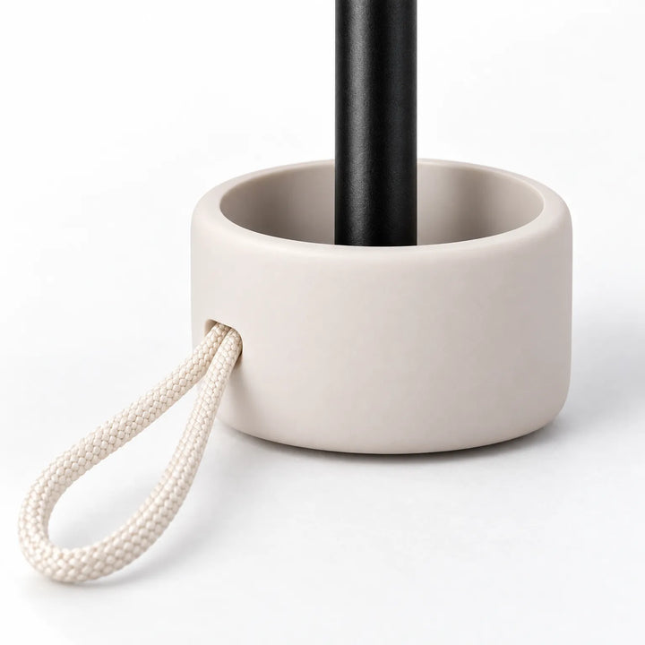 Close-up van het handvat van de paraplu: een beige kapje rond de zwarte steel met een gevlochten crèmekleurig koordlusje. 5