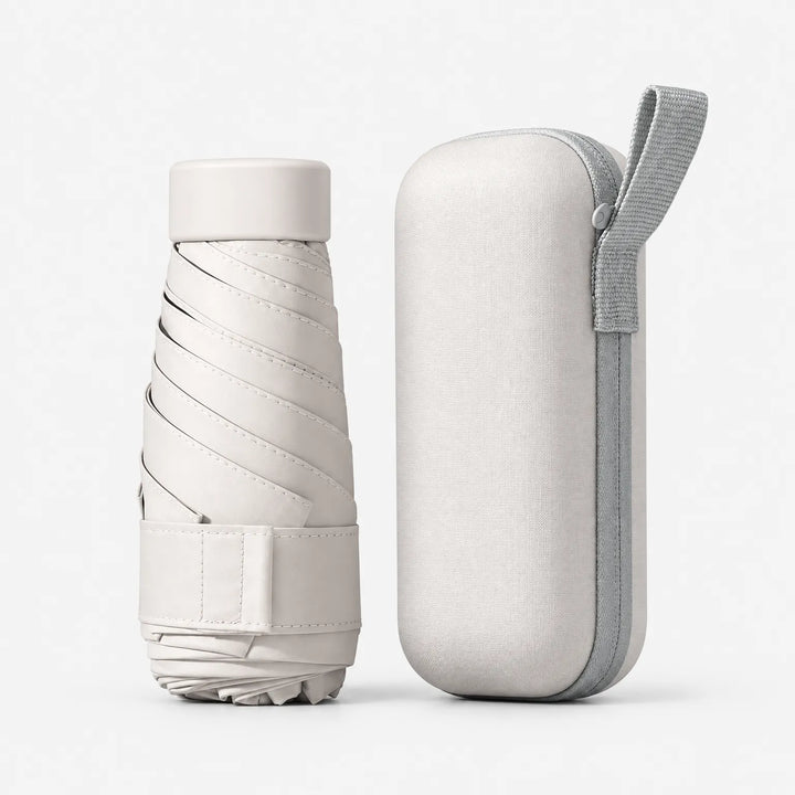 Dichtgevouwen crèmekleurige paraplu met klittenbandsluiting naast het bijpassende etui met grijs polsbandje. 6
