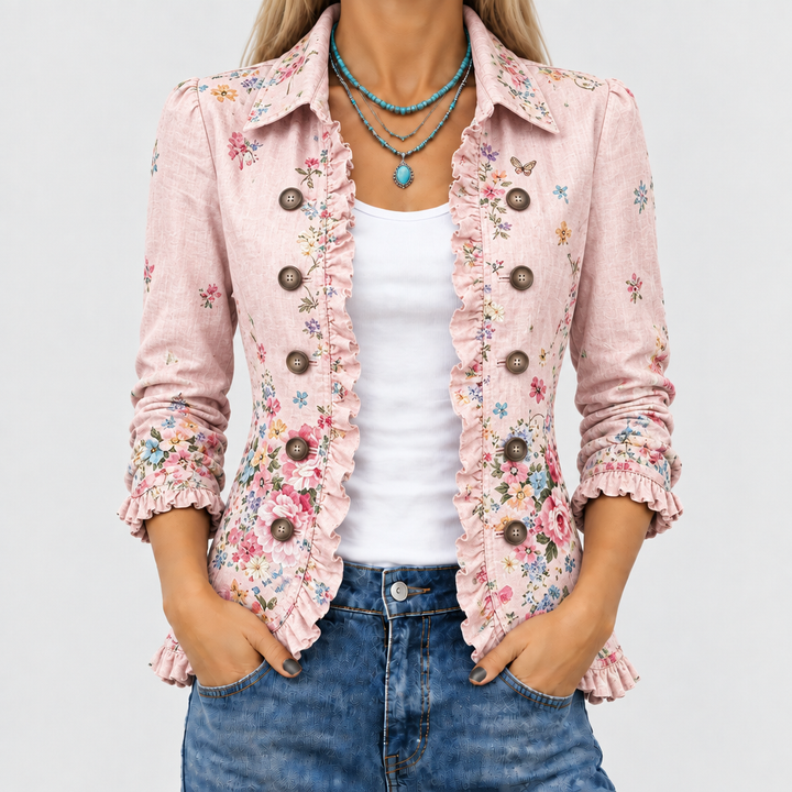 Close-up van het roze jasje met bloemenprint, ruches langs de open voorkant en knopen, gedragen over wit topje en jeans. 1