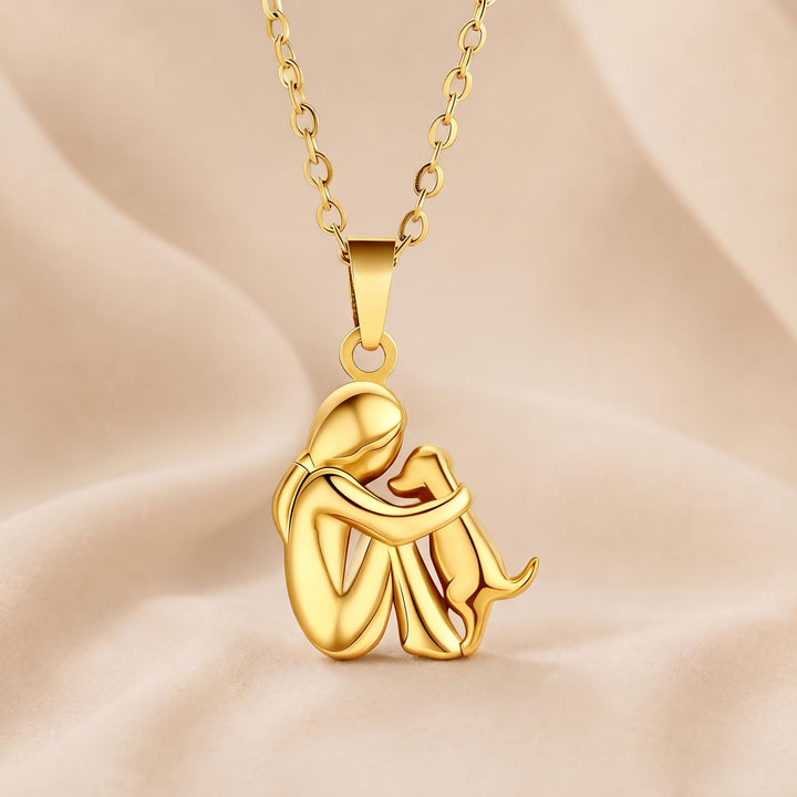 Volledig goudkleurige hanger van een zittende figuur met een hond, aan een goudkleurige schakelketting op zachte beige stof. 5