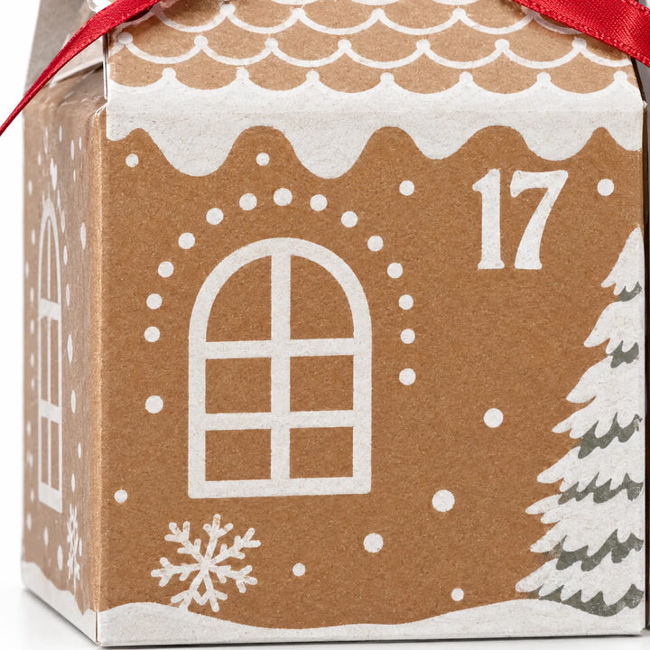 Close-up van een kraftpapieren huisdoosje met wit bedrukt boograam, sneeuwvlok, besneeuwde dennenboom en golvend dak, met rode strik bovenaan. 3