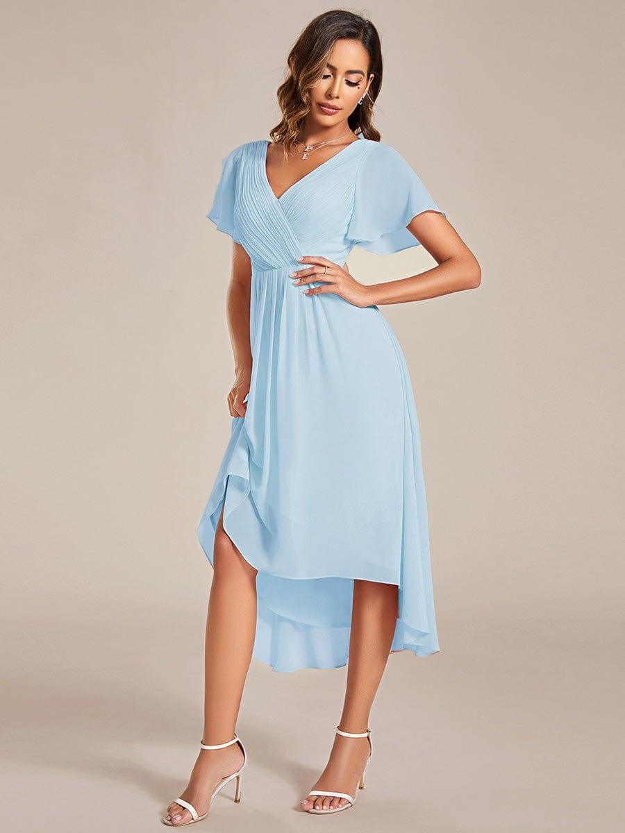 Model in lichtblauwe jurk met hand op de heup, tilt de wijd uitlopende chiffon rok iets op. 88